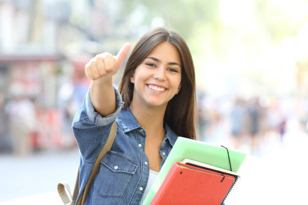 Happy student posing with thumbs up looking at you in the street