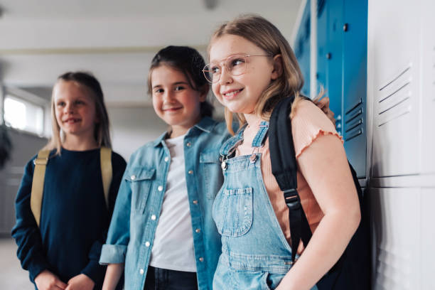 three smiling school children standing in front of lockers in school corridor